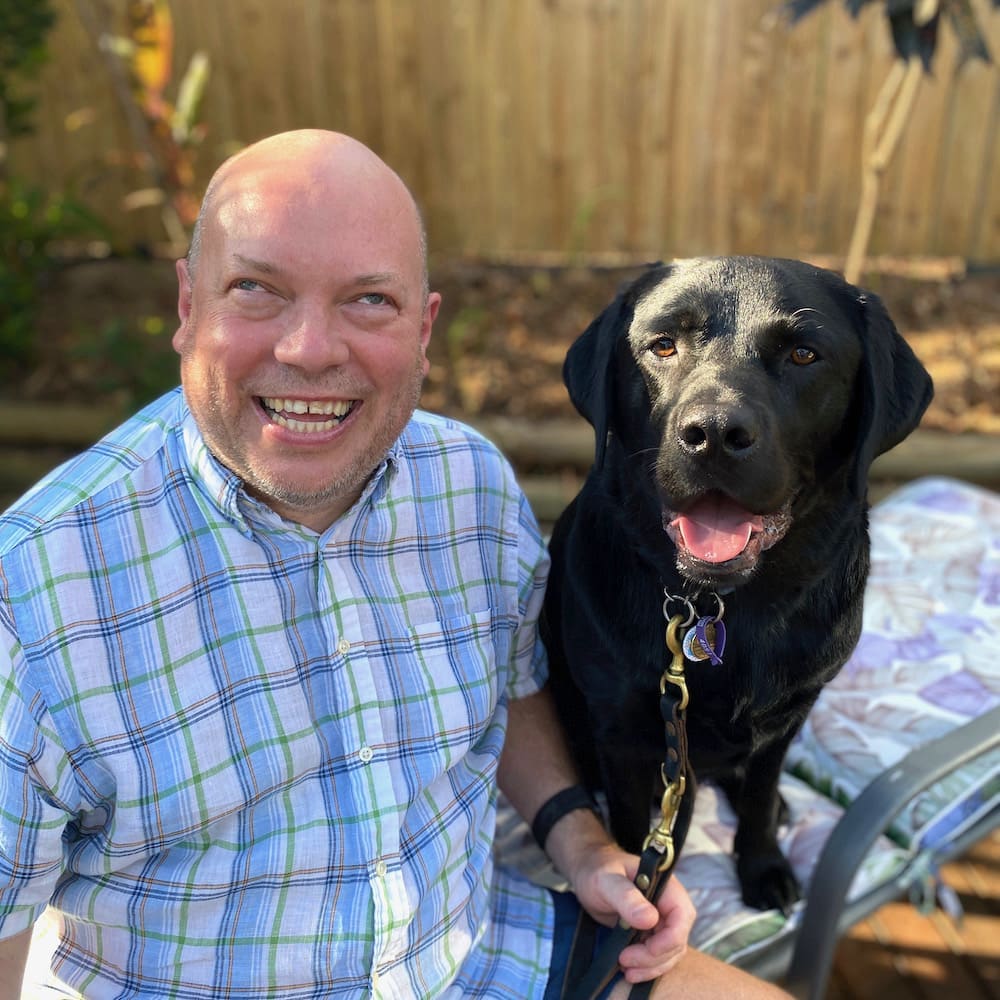 Man smiling with black Labrador outdoors.