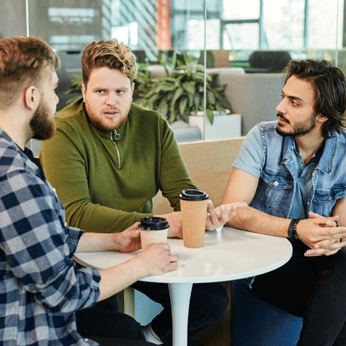 Three men discussing around a table with coffee cups.