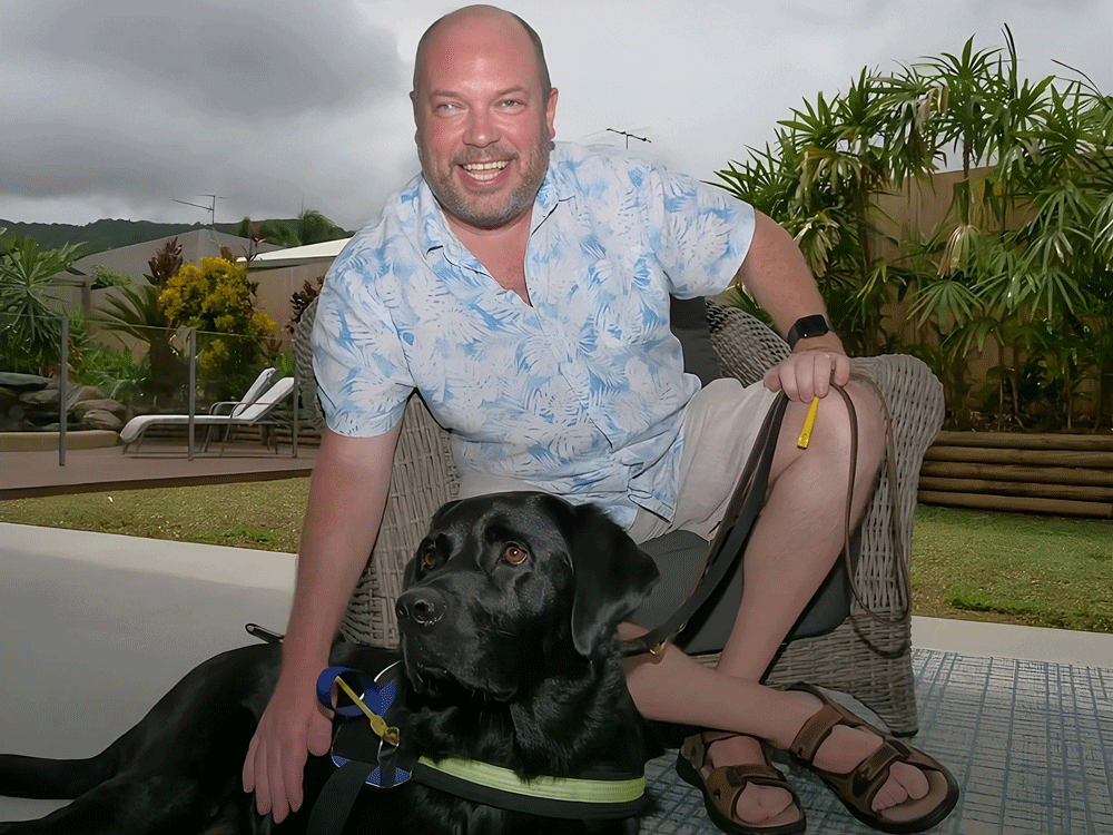 Man with guide dog outdoors, smiling.